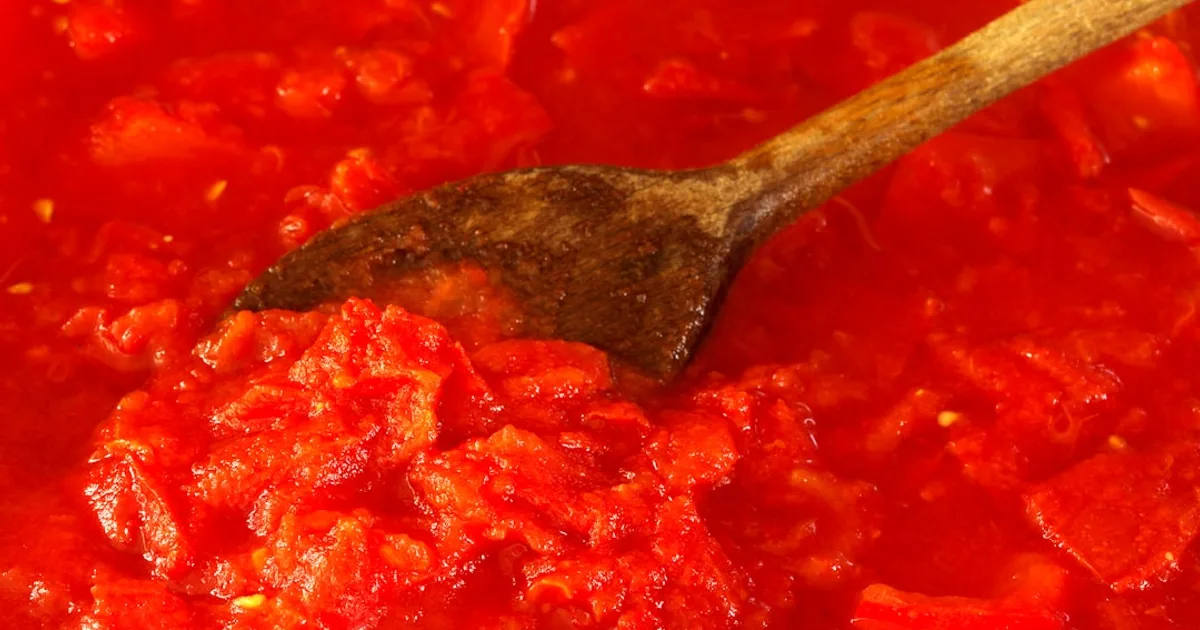 Tomato sauce being stirred with a wooden spoon.