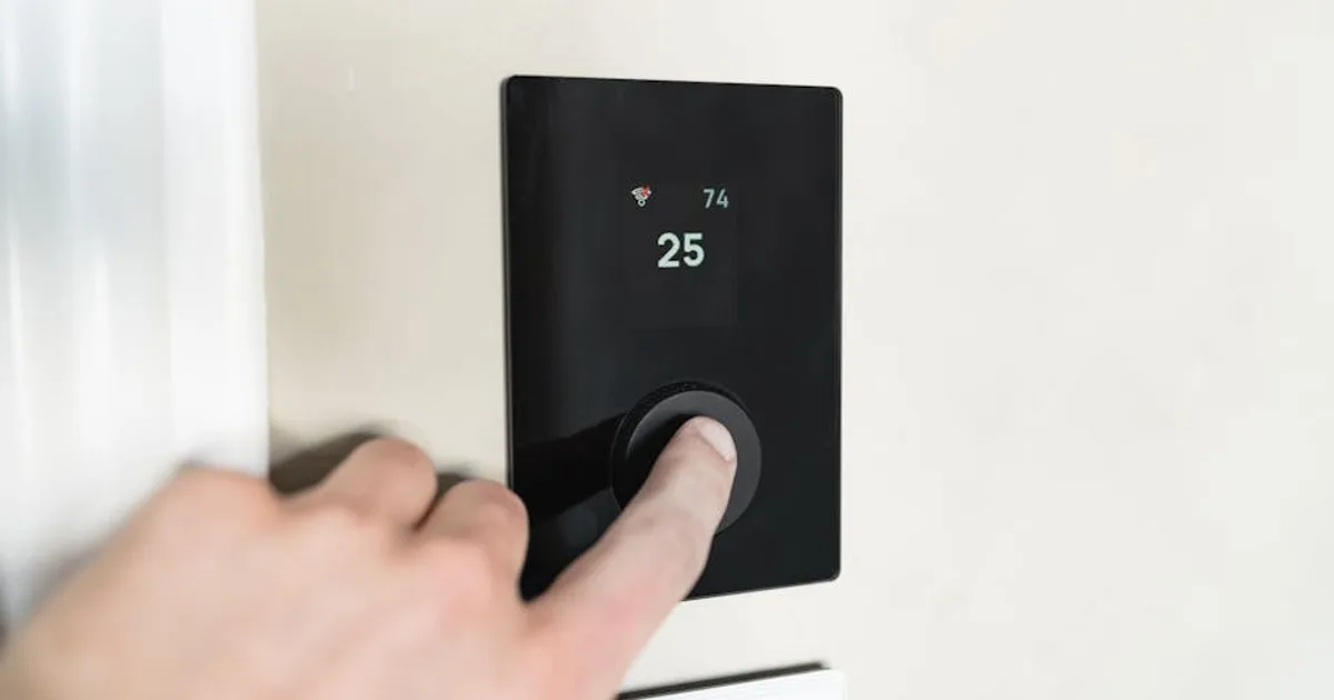 Close-up of a hand adjusting a sleek, modern smart thermostat on a wall.