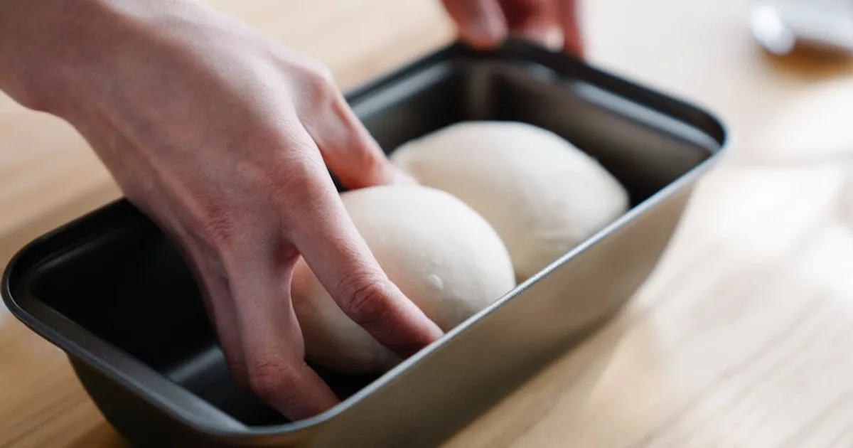 Close-up of hands placing dough balls in a tray, ready for baking.