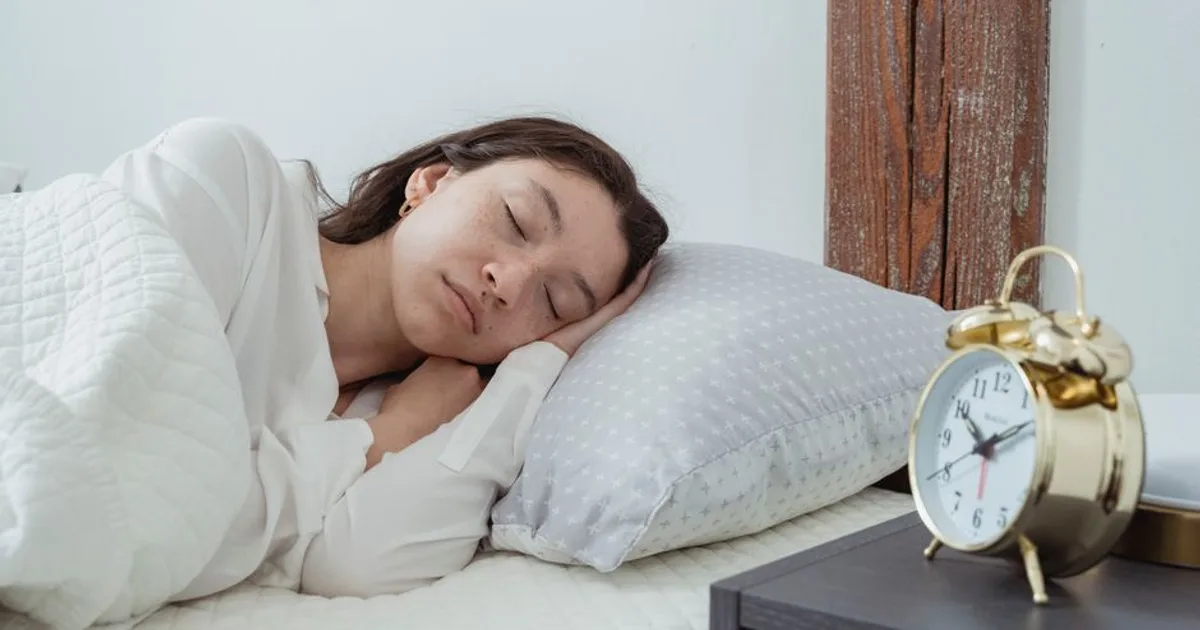 Young calm female with dark hair lying on side with hand under head on white comfortable bed under blanket while sleeping in morning time