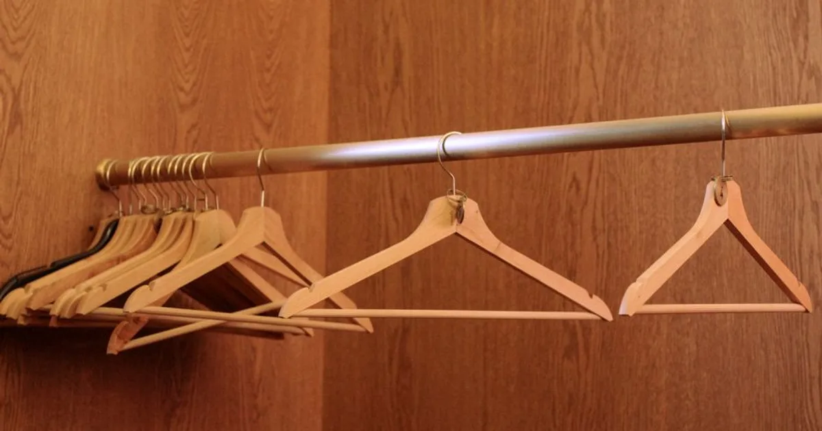 A row of wooden hangers on a metal rod in an empty, wood-paneled closet.
