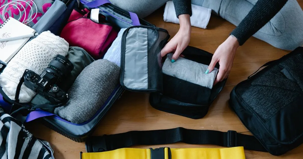 A woman arranging clothes and accessories into a suitcase, preparing for travel.