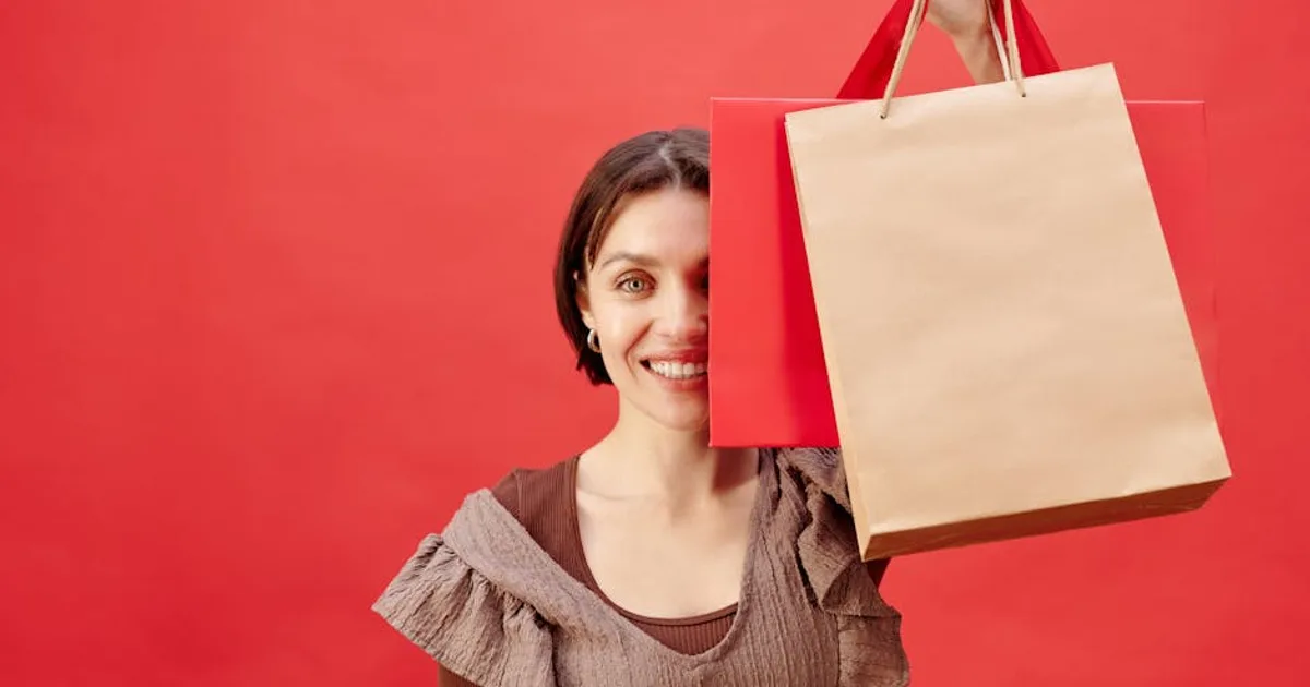 Joyful woman holding shopping bags against a bright red backdrop, expressing excitement.