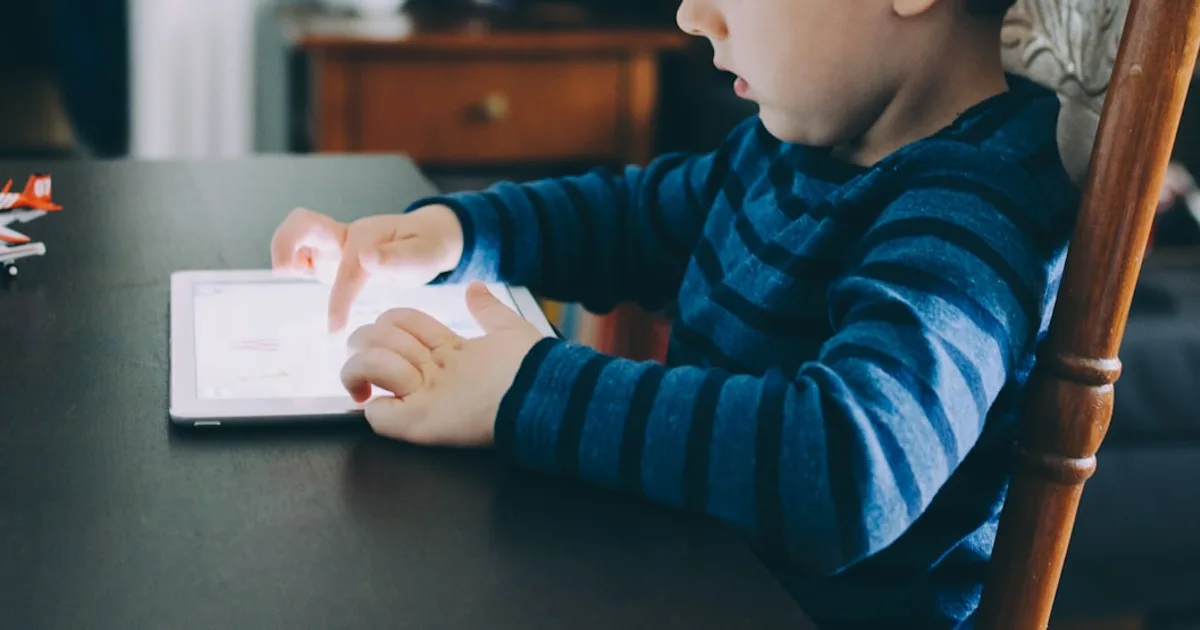 boy sitting on chair beside table using tablet computer